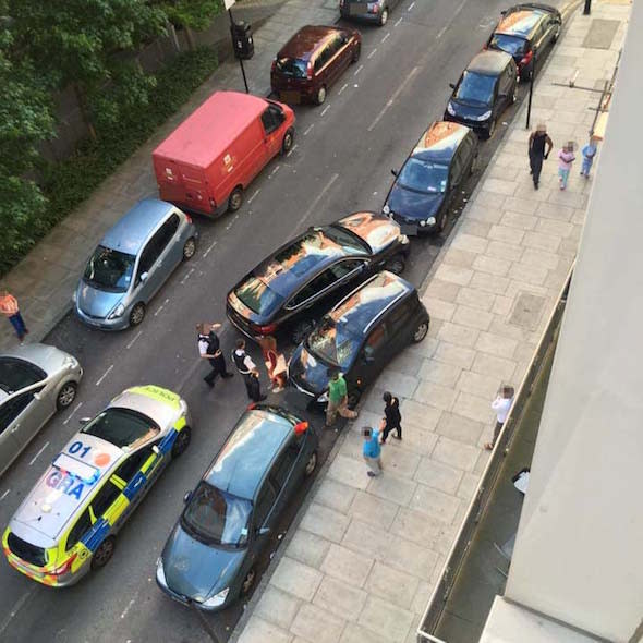 PIC FROM MERCURY PRESS (PICTURED: POLICE IN ATTENDANCE OVER THE PARKING ROW BETWEEN A HATCHBACK OWNER (WOMAN IN MAROON DRESS, CENTRE) AND BMW DRIVER (MAN IN WHITE SHIRT, RIGHT))  A heated hour-long parking stand-off erupted in London when a female driver raced over the PAVEMENT almost hitting children to wedge her car in the gap as another motorist tried to park there. Mark Williamson took photos of the row in what he thinks is one of the most notorious parking areas in London on the boundary between Isle of Dogs and Canary Wharf. On Friday (JUNE 24), Mark was on his way home when he watched a male BMW driver attempting to park in a spot outside Markâ€™s apartment. But as he halfway through his manoeuvre, a lady in a black hatchback raced along the pavement, narrowly missing eight children playing, and sneaked the carâ€™s nose in the spot. Both drivers got out of their cars sparking a heated row that prompted police to be called when neither driver had budged more than 30 minutes later. SEE MERCURY COPY