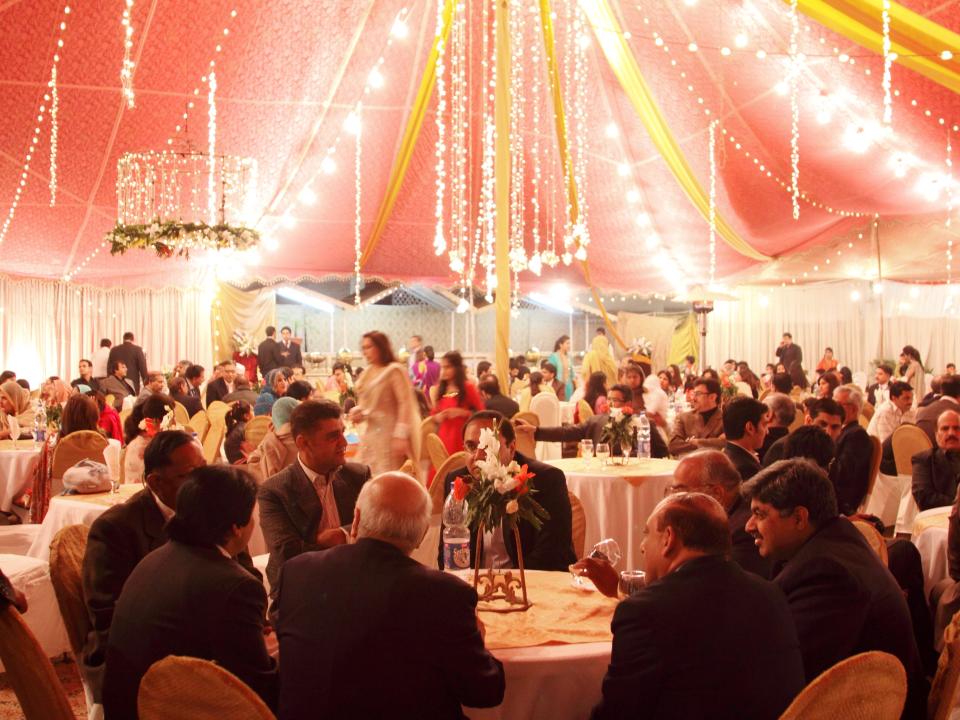 A large group of people under a peach-colored tent for a wedding ceremony