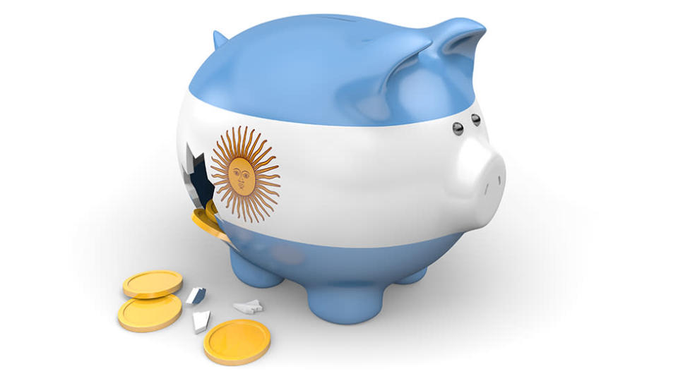Cerdito de ahorro con los colores de la bandera argentina roto, con monedas saliendo