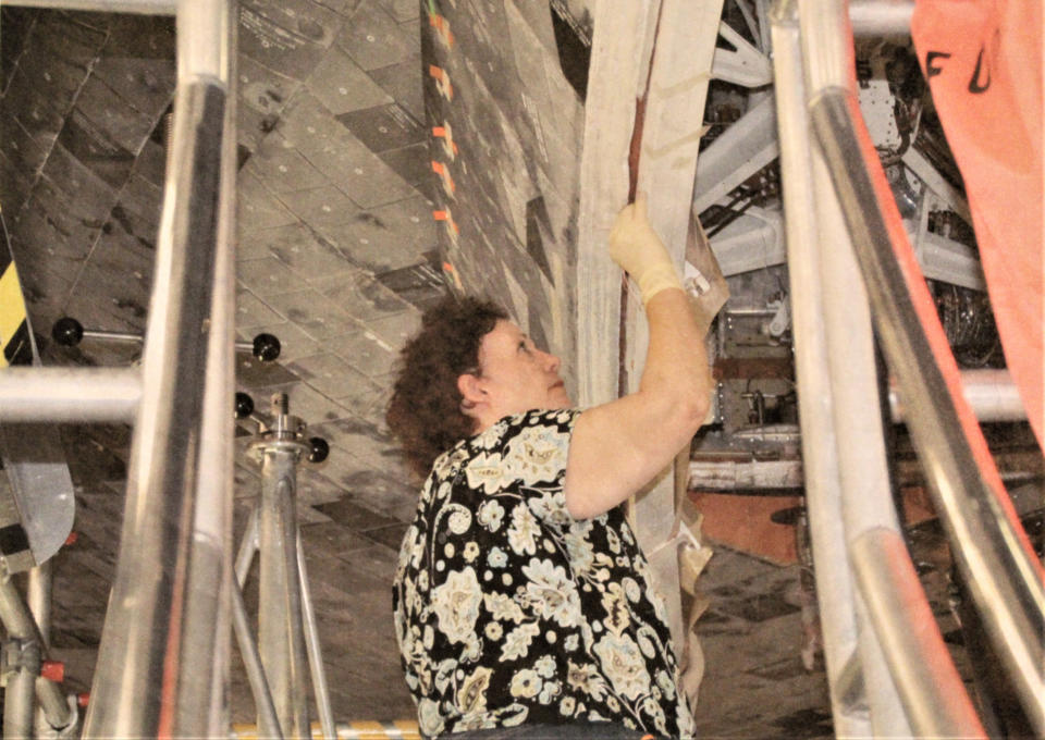 a woman stands near the underside of the space shuttle working