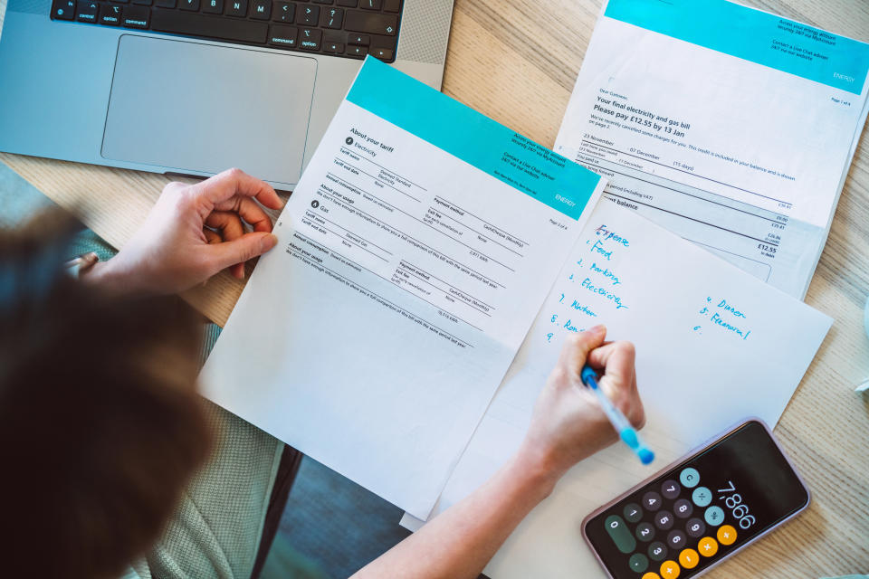 Person at desk working on finances with documents, laptop, and calculator showing 7866. Writing a to-do list that includes "pay bills" and "budget."