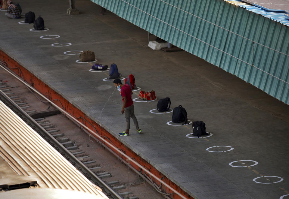 A man spits water on rail tracks as passengers line up their bags on the railway station platform to reserve their spots in boarding queue in New Delhi, India, Tuesday, May 12, 2020. India is reopening some of its colossal rail network as the country looks at easing its nearly seven-week strict lockdown amid an increase in coronavirus infections. (AP Photo/Manish Swarup)