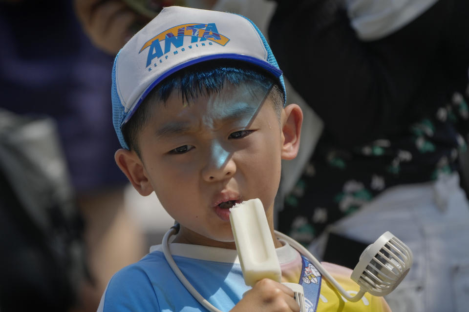 A boy wearing an electric fan eats an ice cream near the Forbidden City on a sweltering day in Beijing, Friday, July 7, 2023. Earth's average temperature set a new unofficial record high on Thursday, the third such milestone in a week that already rated as the hottest on record. (AP Photo/Andy Wong)