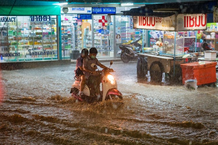 People ride a motorbike through rain and heavy floods amid city lights