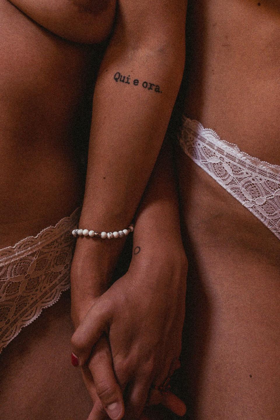 Close-up of the couple holding hands, with one hand showing a "qui e ora" tattoo