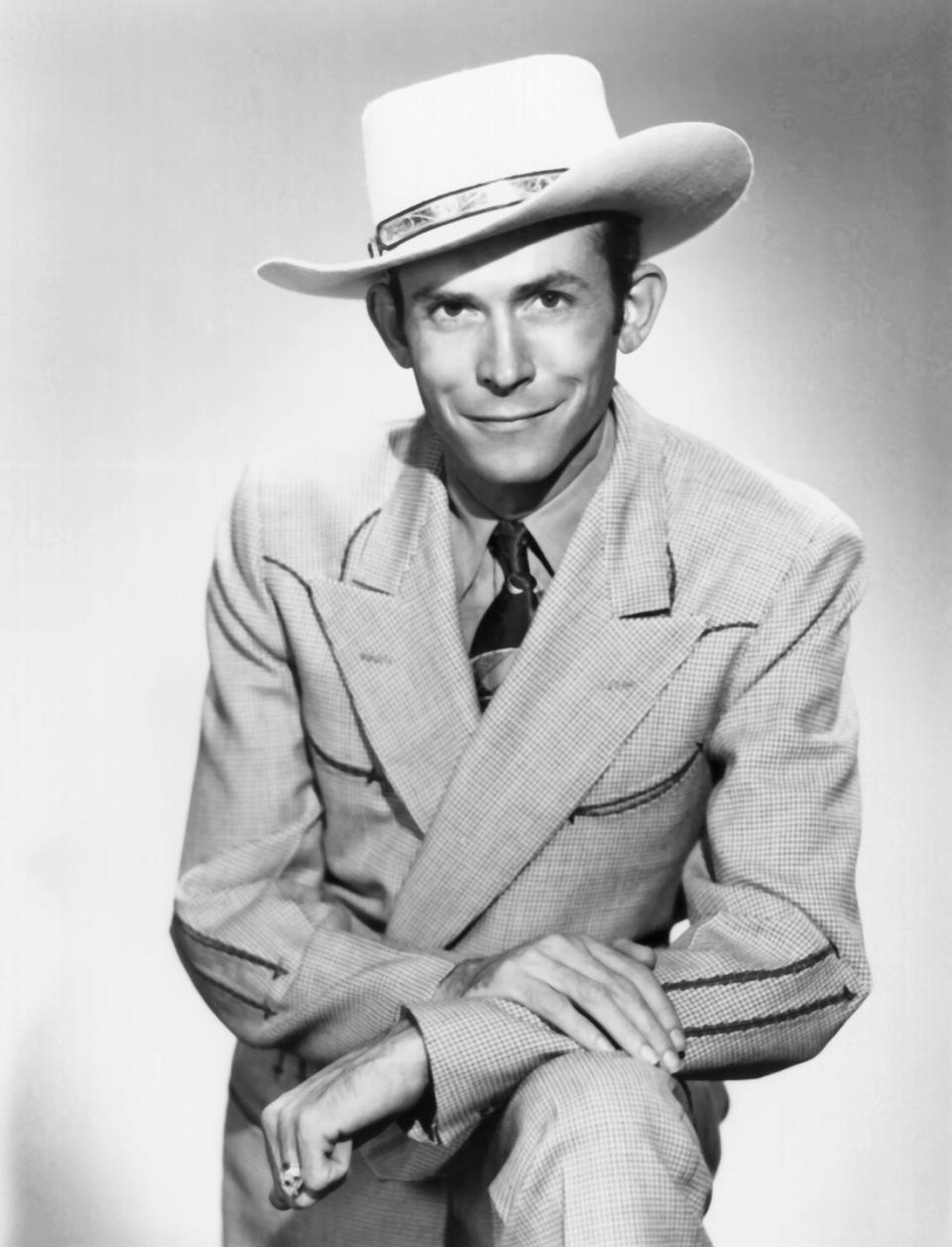 hank williams standing his arms folded on top of his left knee and smiling