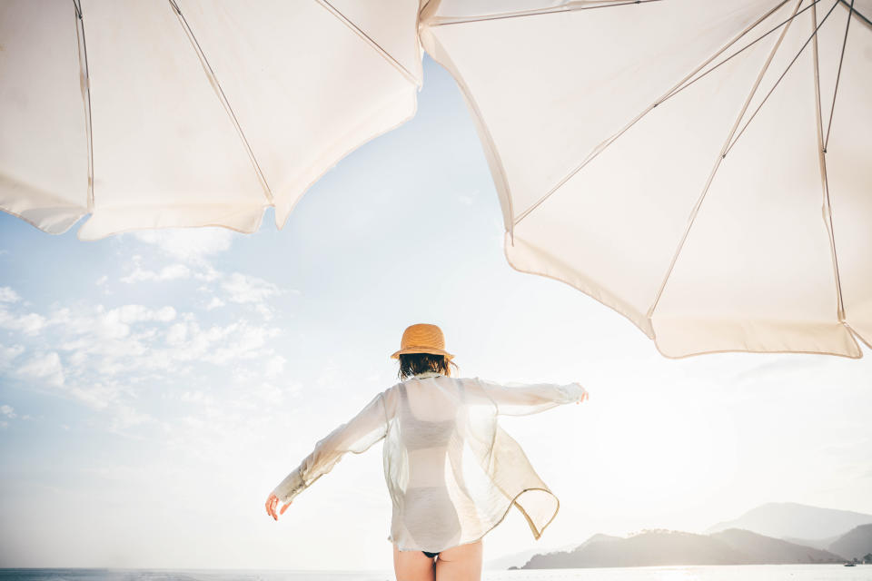 Back view of woman walking on beach.Darker clothing absorbs more UV than lighter colours, making it more protective. (Getty)
