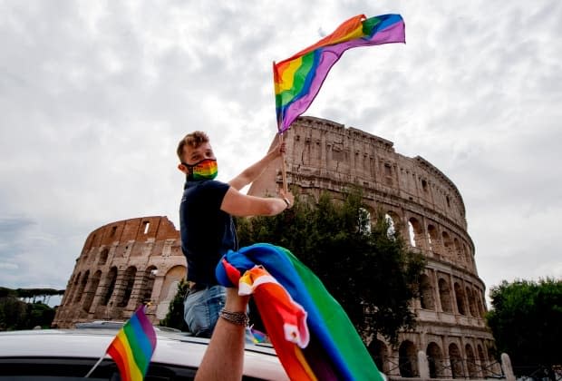 A man waves a Pride flag past the Colosseum during a Rome Pride flash mob on June 13, 2020 in Rome. Lifelines for LGBT youth in Italy and elsewhere in Europe are thinly stretched amid the COVID-19 pandemic. (Tiziana Fabi/AFP via Getty Images - image credit)