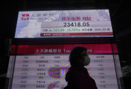 A woman wearing face mask walks past a bank electronic board showing the Hong Kong share index in Hong Kong Monday, April 6, 2020. Asian shares and U.S. futures have rebounded as investors grasped at threads of hope that the battle against the coronavirus pandemic may be making some progress in some hard-hit areas.(AP Photo/Vincent Yu)