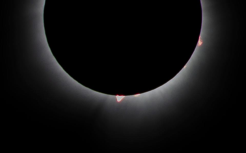 Red prominences appear to jut from the edge of the moon during the total solar eclipse at Switchyard Park on April 8, 2024.