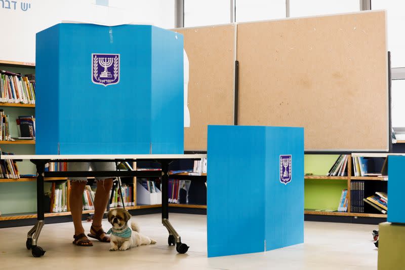 A dog rests while its owner stands behind a voting booth as he casts his ballot in Israel's general election at a polling station in Tel Aviv