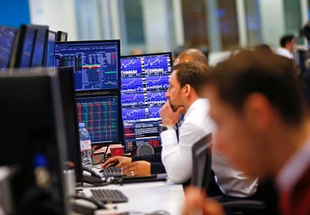 Traders work at their desks whilst screens show market data at CMC Markets in London