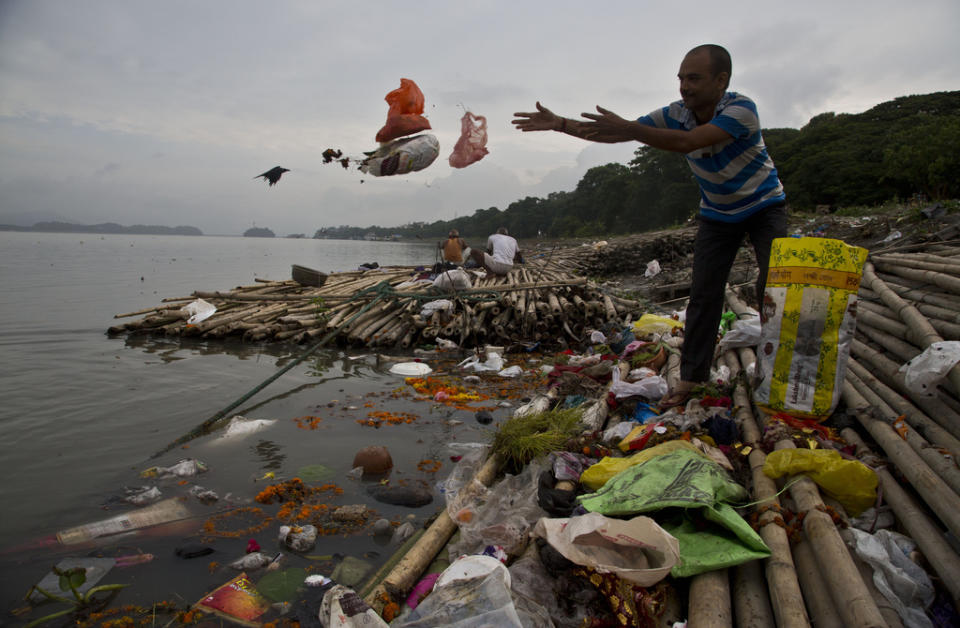 一名印度教信徒將鮮花和塑膠袋扔進印度高哈蒂的雅魯藏布江，這些塑膠最終將流進大海。（圖／美聯社）