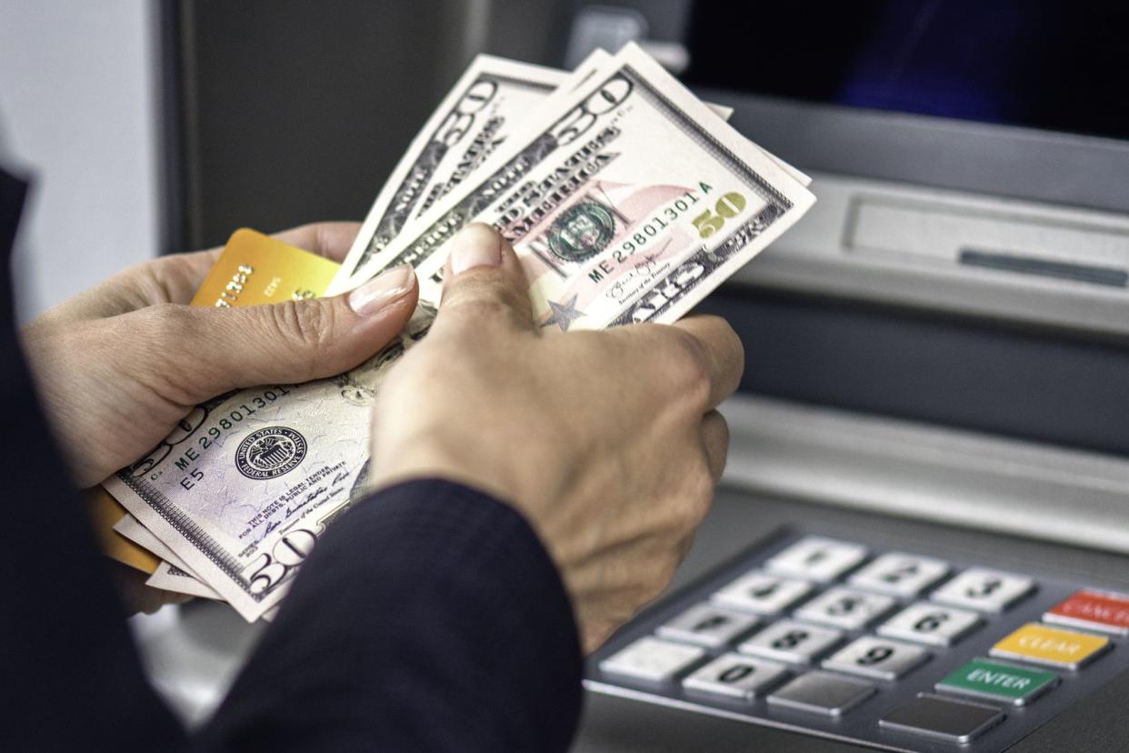 hands holding $50 bills in front of atm