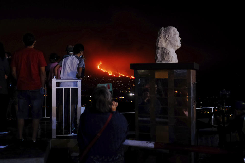 People watch the volcano as it continues to spew lava on the Canary island of La Palma, Spain on Saturday, Oct. 9, 2021. A new river of lava has belched out from the La Palma volcano, spreading more destruction on the Atlantic Ocean island where molten rock streams have already engulfed over 1,000 buildings. The partial collapse of the volcanic cone has sent a new lava stream heading toward the western shore of the island. (AP Photo/Daniel Roca)