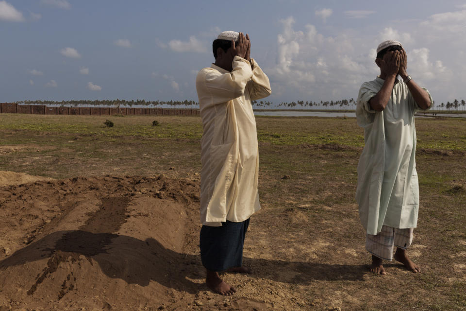 Two men are seen mourning at the funeral of a woman who died from stomach disease.