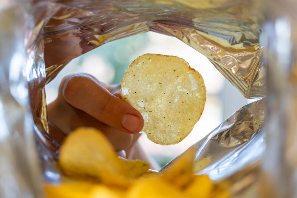 Person's hand picking up a potato chip from an open bag, view from inside the bag