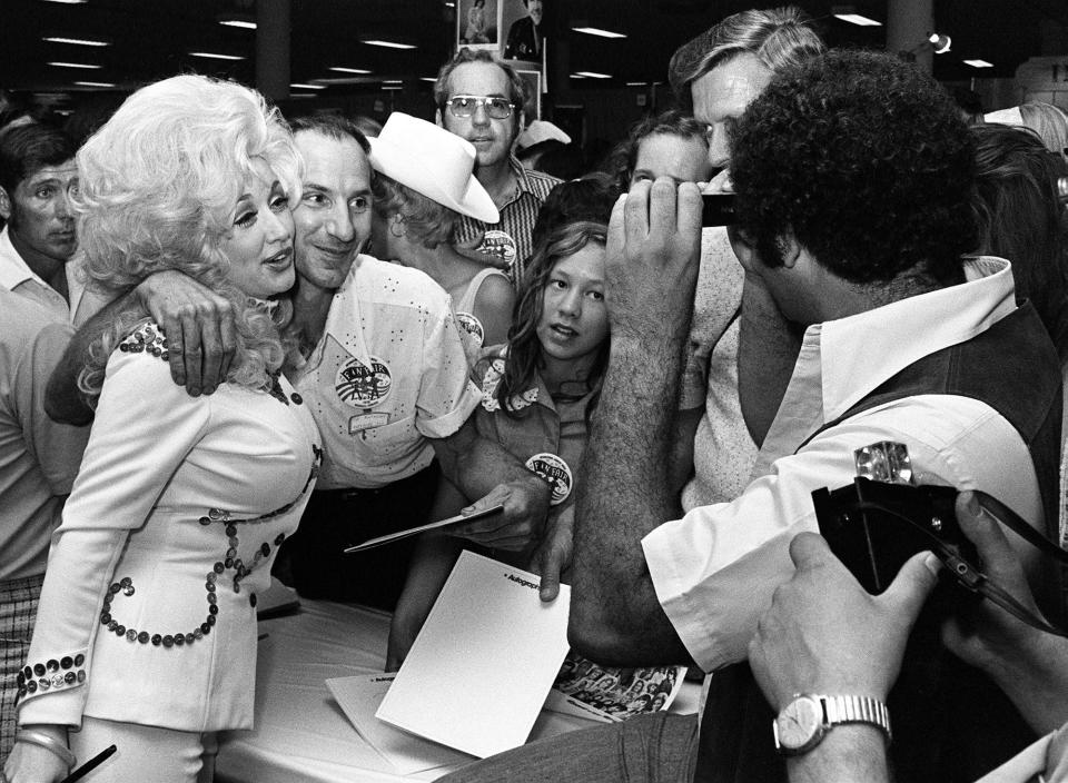 Dolly Parton, left, poses with a fan as she signs autographs at her booth in the Municipal Auditorium during Fan Fair on June 10, 1976.