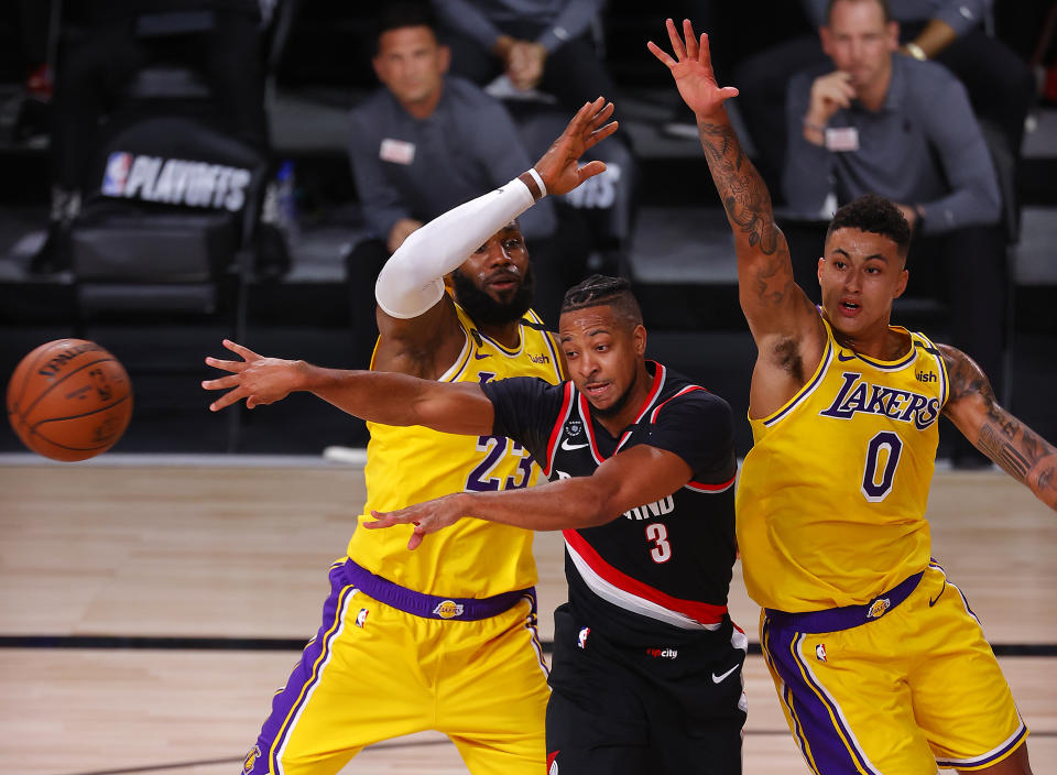 CJ McCollum, center, of the Portland Trail Blazers, passes the ball as Los Angeles Lakers defenders LeBron James, left, and Kyle Kuzma, right, defend during the first half of Game 1 of an NBA basketball first-round playoff series, Tuesday, Aug. 18, 2020, in Lake Buena Vista, Fla. (Mike Ehrmann/Pool Photo via AP)