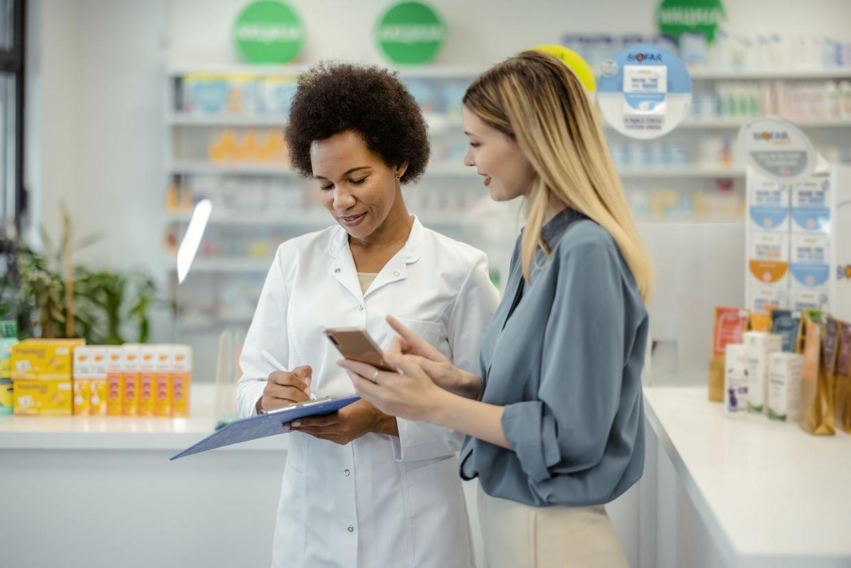 Pharmacy Drugstore: Smiling Female Customer Showing Mobile Phone to Black Female Chemist in Pharmacy