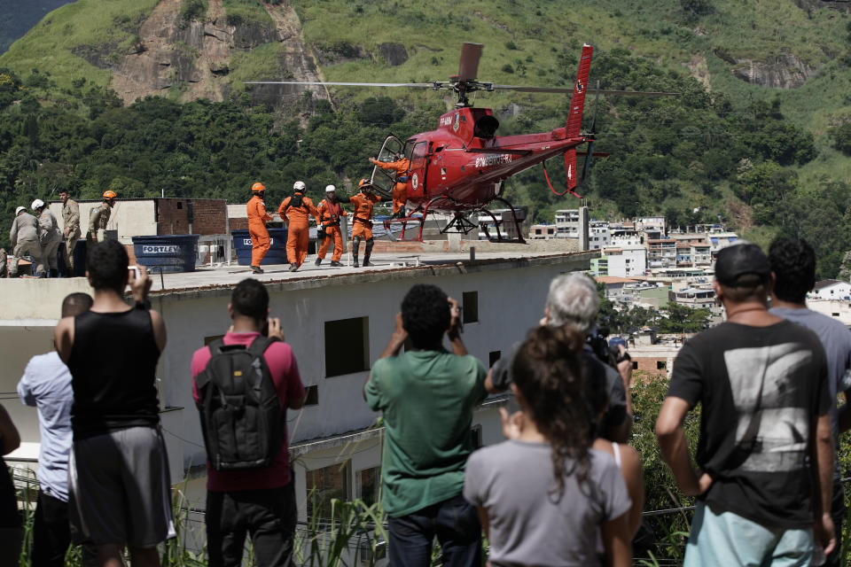 Residents watch as a helicopter prepares to take off carrying an injured woman rescued from the rubble of two buildings that collapsed in the Muzema neighborhood, Rio de Janeiro, Brazil, Friday, April 12, 2019. The collapse came in a western part of the city that was particularly hard hit by heavy rains this week that caused massive flooding. (AP Photo/Leo Correa)