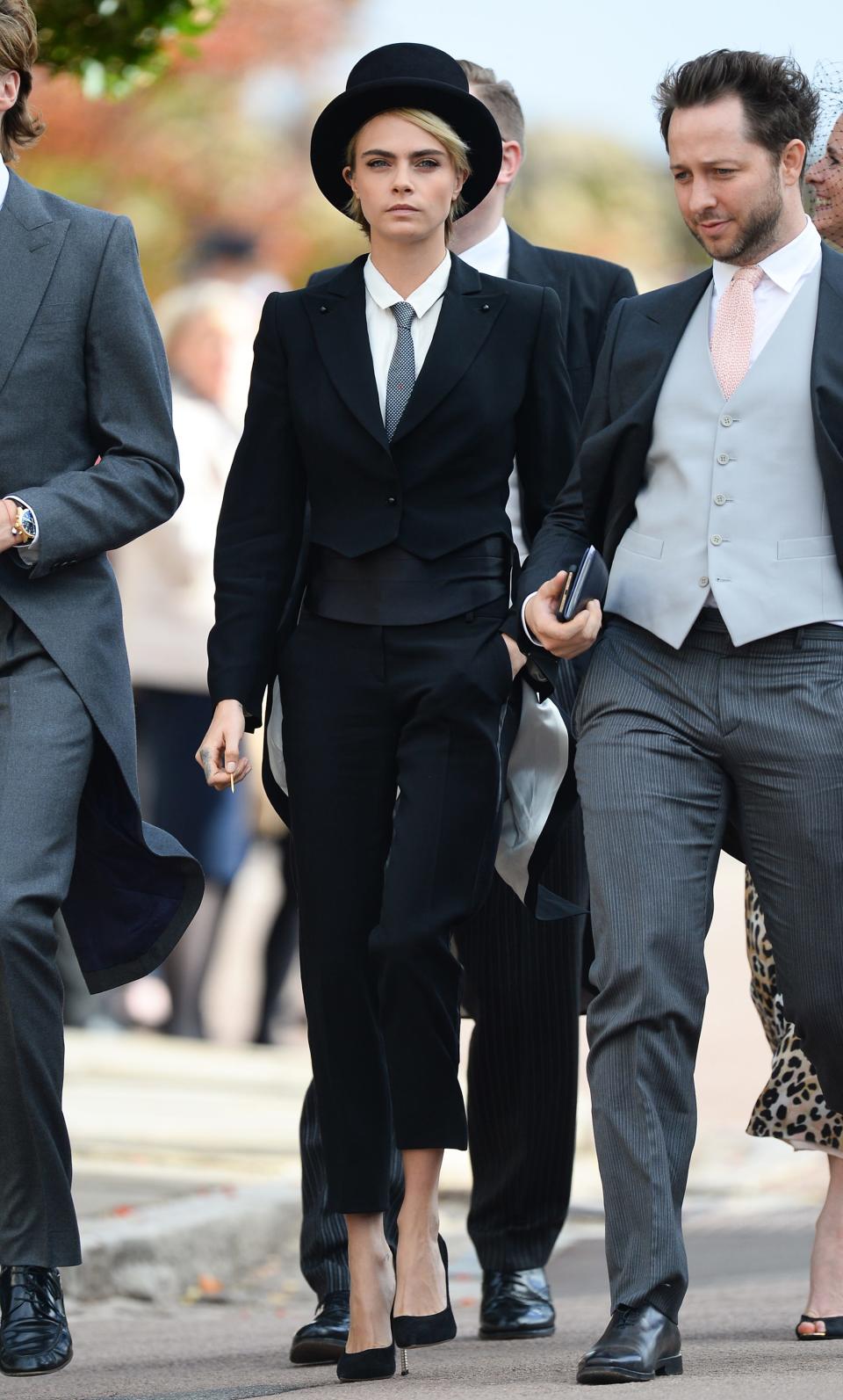 Cara Delevigne walks in a suit and top hat.
