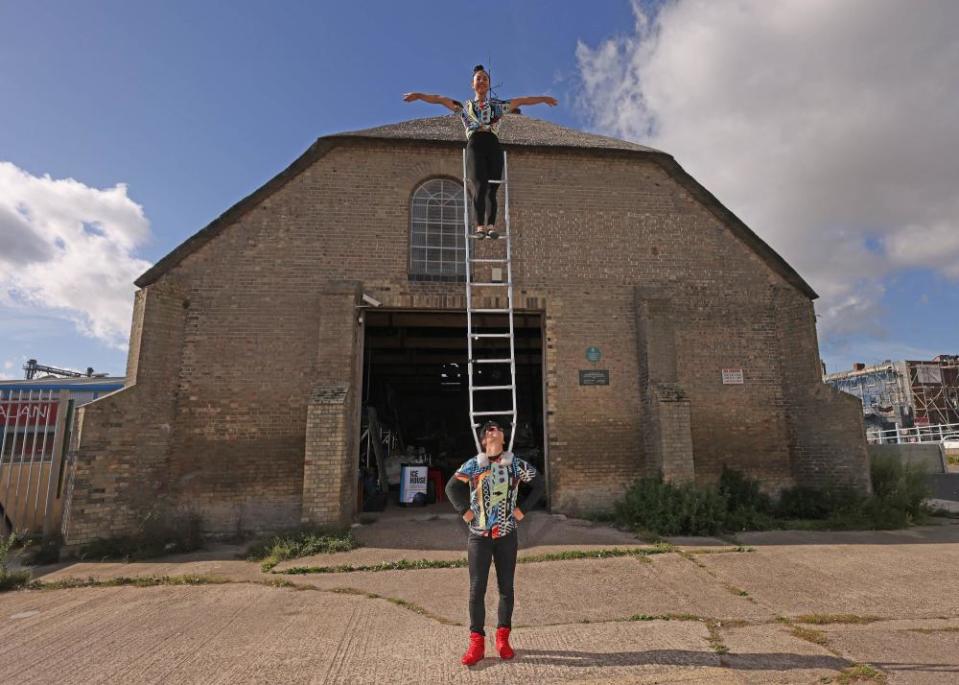 Circus tumblers performing with a ladder outside a thatch-roofed ice house