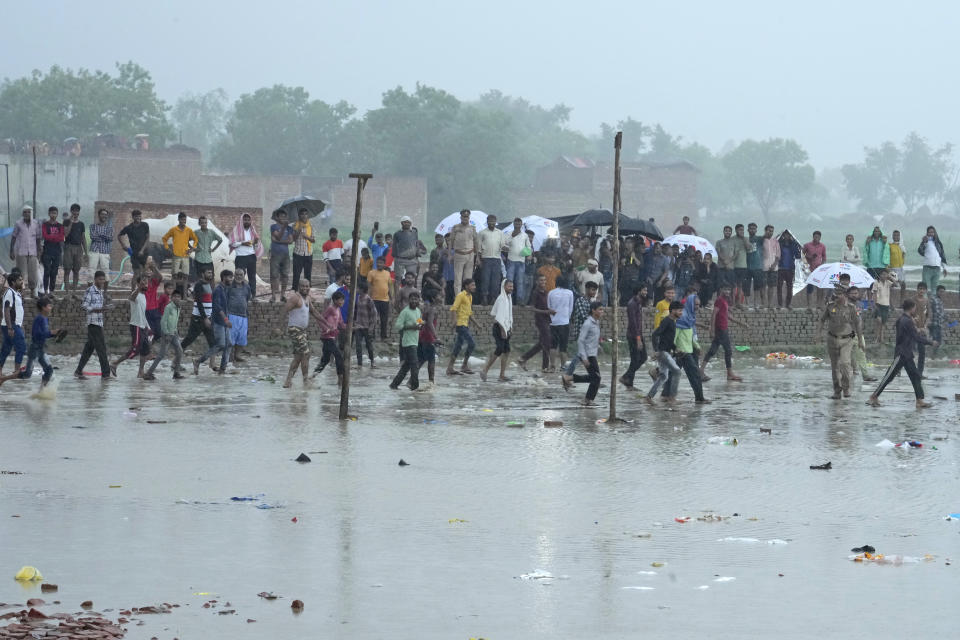 Villagers crowd at the site of Tuesday's stampede as it rains in Hathras district, Uttar Pradesh, India, Wednesday, July 3, 2024. Severe overcrowding and a lack of exits contributed to a stampede at a religious festival in northern India, authorities said Wednesday, leaving more than 100 people dead as the faithful surged toward the preacher to touch him and chaos ensued. (AP Photo/Rajesh Kumar Singh)