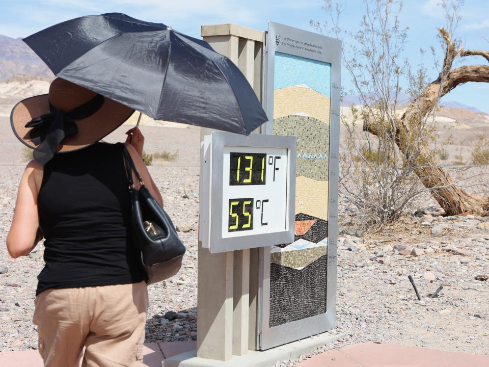 A woman stands near a digital display of an unofficial heat reading at Furnace Creek Visitor Center during a heat wave in Death Valley National Park, California, on July 16, 2023.