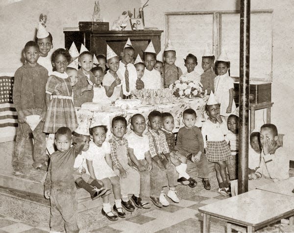 James McCoy's birthday party at the Pat Wee Nursery and Kindergarten in Frenchtown in 1962. Ronald McCoy in front of cake with bird on hat and wearing bow tie. Brother James, two spots to the right of Ronald, also with a bird on front of hat. Standing 3rd from right is Alexis McMillan (family owns Economy Drug Store in Frenchtown).