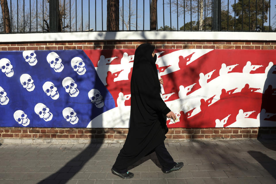 A mourner walk back from a funeral ceremony for Iranian Gen. Qassem Soleimani and his comrades, who were killed in Iraq in a U.S. drone attack on Friday, passing graffiti on the wall of the former U.S. Embassy in Tehran, Iran, Monday, Jan. 6, 2020. A push led by pro-Iran factions to oust U.S. troops from Iraq is gaining momentum, bolstered by a Parliament vote in favor of a bill calling on the the government to remove them. But the path forward is unclear. (AP Photo/Vahid Salemi)