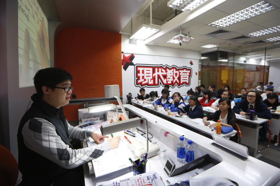 In this Dec. 9, 2013 photo, English grammar tutor Tony Chow, left, gives a lesson to his students in a classroom of Modern Education in Hong Kong. The 30-year-old teaches English grammar to thousands of secondary school pupils, who attend his after-school lessons or watch video replays of them at Modern Education’s 14 branches. Chow is a celebrity tutor in Hong Kong, where there’s big money to be made offering extracurricular lessons to parents desperately seeking an edge for their children preparing for the city’s intense public entrance exam for university. (AP Photo/Kin Cheung)