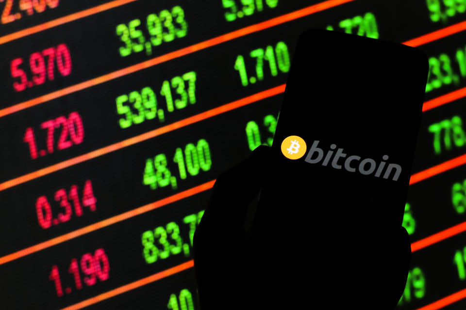 POLAND - 2020/03/13: In this photo illustration, a Bitcoin cryptocurrency logo is displayed on a smartphone.  Share prices in the background as stock markets fall around the world.  (Photo by Filip Radwanski/SOPA Images/LightRocket via Getty Images)