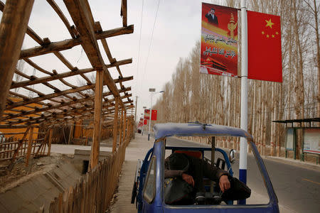 A man rests under a poster showing Chinese President Xi Jinping in the village of Jiya near Hotan, Xinjiang Uighur Autonomous Region, China, March 21, 2017. REUTERS/Thomas Peter