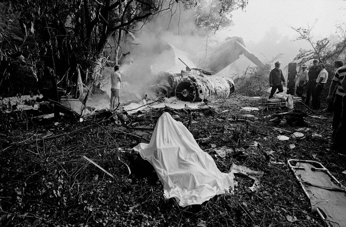 A shroud covers the body of a deceased passenger still strapped in an airplane seat as the tail section of Eastern Flight 212 smolders in the background on Sept. 11, 1974.