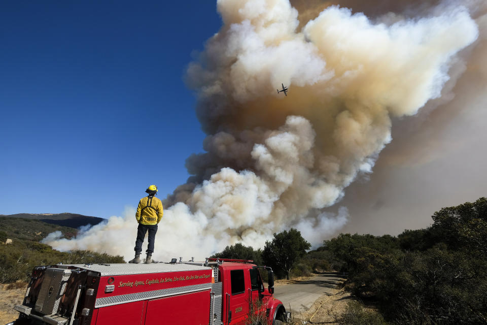 A firefighter watches on his fire engine as smoke rises from a wildfire Wednesday, Oct. 13, 2021, in Goleta, Calif. A wildfire raging through Southern California coastal mountains threatened ranches and rural homes and kept a major highway shut down Wednesday as the fire-scarred state faced a new round of dry winds that raise risk of flames. The Alisal Fire covered more than 22 square miles (57 square kilometers) in the Santa Ynez Mountains west of Santa Barbara. (AP Photo/Ringo H.W. Chiu)