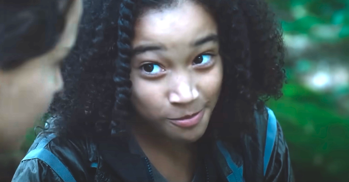 Amandla Stenberg, dressed casually, gazes to the side with a slight smile in an outdoor setting