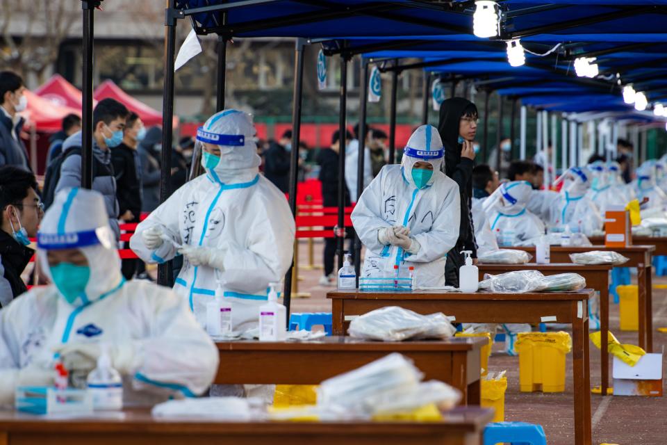 Rows of medical personnel prepare COVID-19 test kits in tented facilities