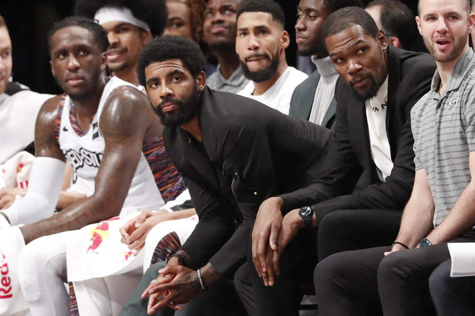 Injured Brooklyn Nets guard Kyrie Irving, center, perches on the edge of his seat during the second half of an NBA basketball gam against the New York Knicks, Thursday, Dec. 26, 2019, in New York. The Knicks defeated the Nets 94-82. (AP Photo/Kathy Willens)