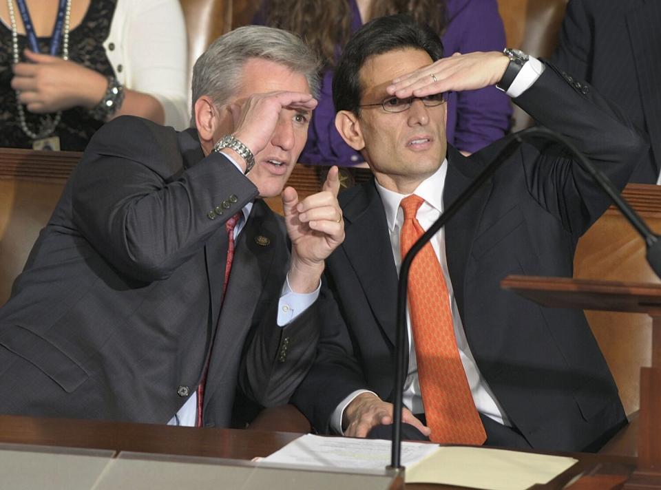 Kevin McCarthy and Eric Cantor sit at a table and look across the House chamber