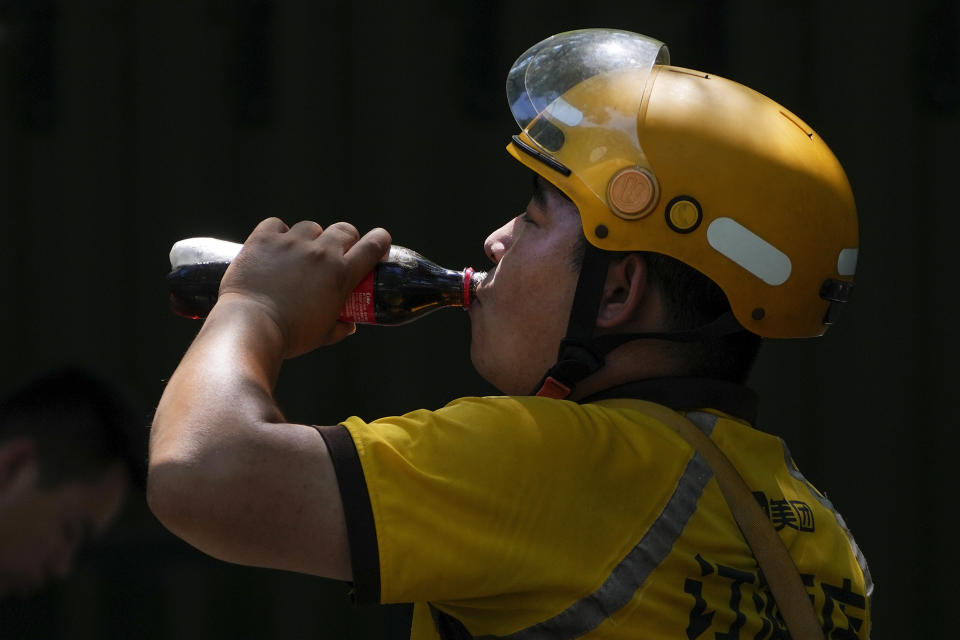 A delivery rider drinks a coke on a sweltering day in Beijing, Monday, July 10, 2023. Rescuers were looking Monday for several people missing in a landslide triggered by torrential rains while employers across much of China were ordered to limit outdoor work due to scorching temperatures as the country struggled with heat, flooding and drought. (AP Photo/Andy Wong)