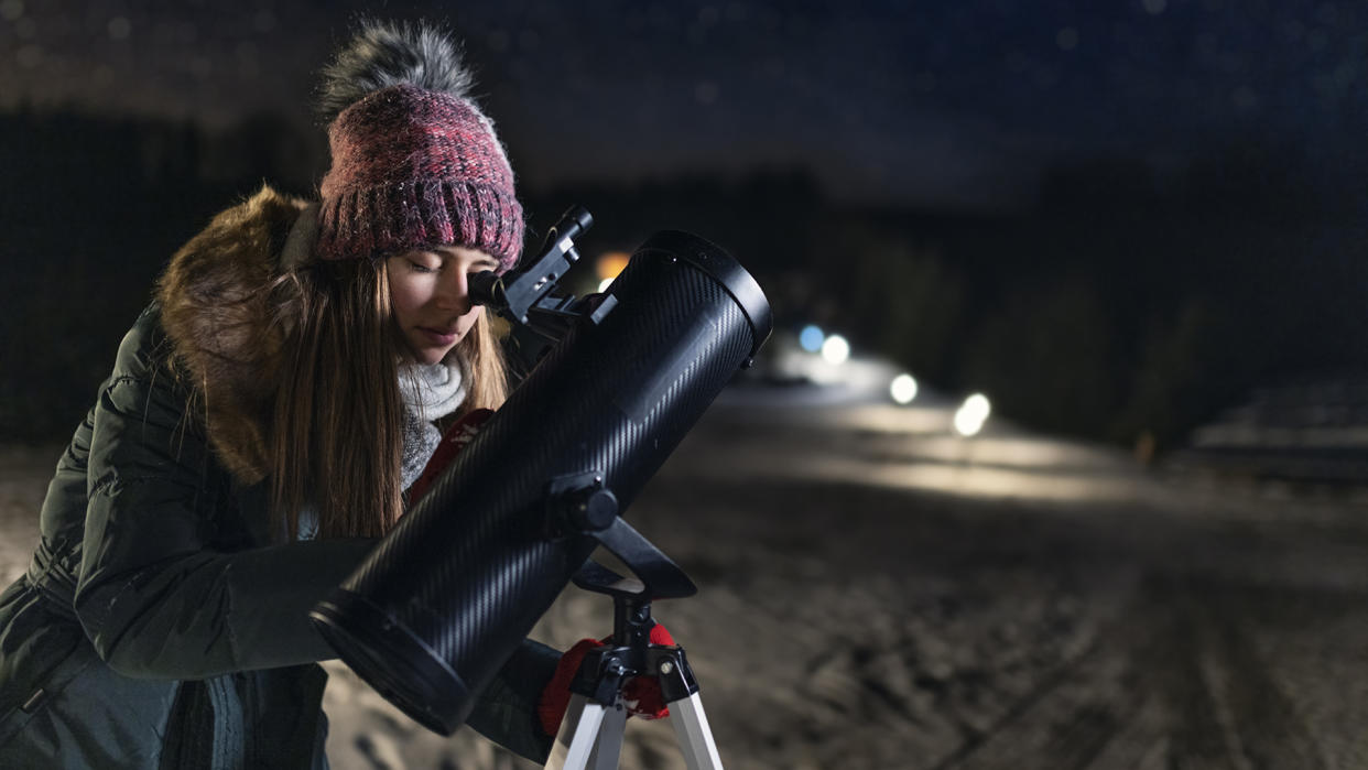  Teenage girl is using the astronomy telescope to observe the the stars at cold winter night. 