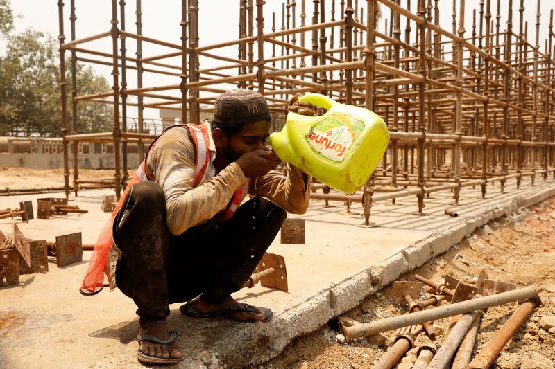 A construction worker drinks water from a container as he takes a break at a construction site during a hot summer day in New Delhi