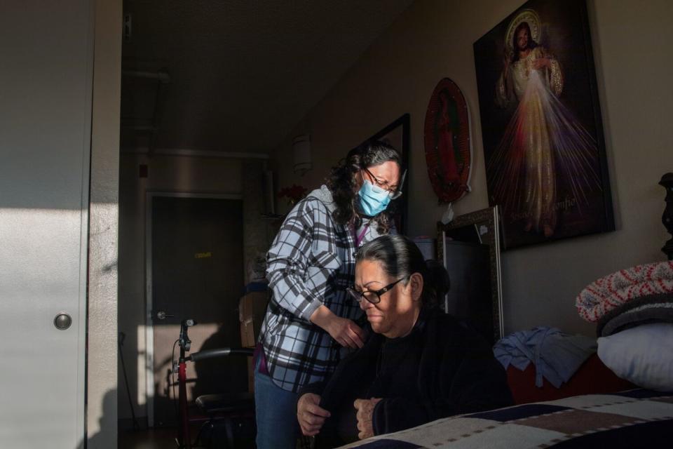 Maria Diaz, left, stands behind Maria Martinez, helping her get dressed.