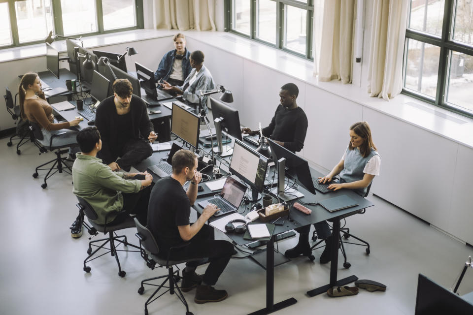 Two rows of young people work at tables set up with four monitors each.(Getty Images)