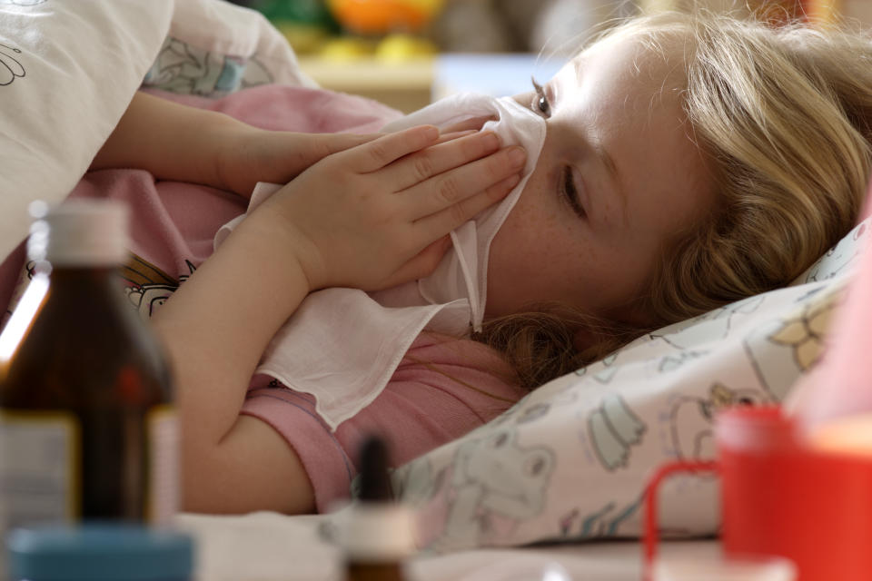 A young child, children lies in bed while sick, blowing into a tissue as she has a weakened immune system. (Photo via Getty Images)