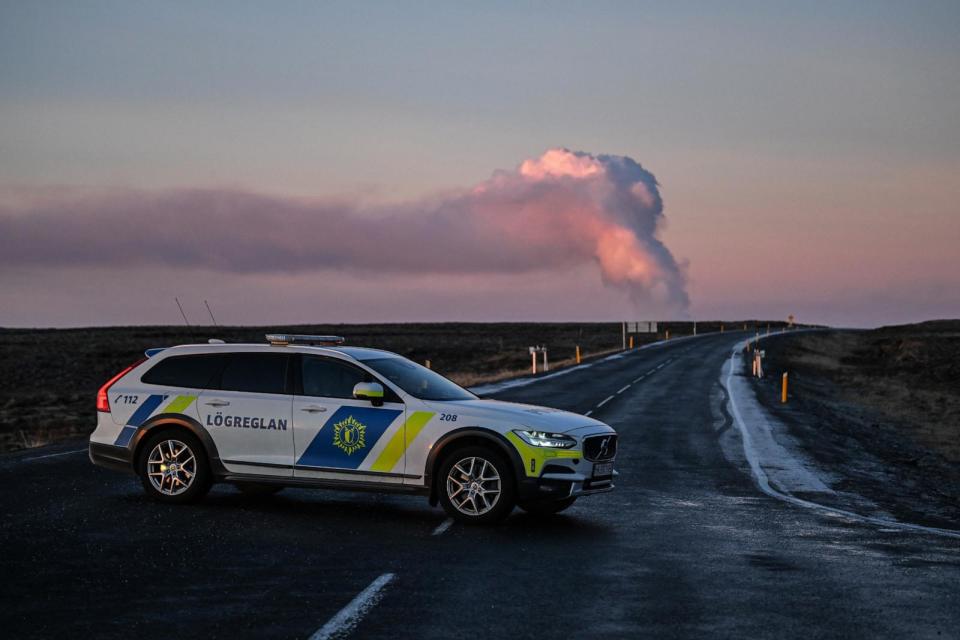 PHOTO: Billowing smoke from a volcanic eruption is seen as a police car blocks the road north of the southwestern Icelandic town of Grindavik, on Jan. 14, 2024.  (Sergei Gapon/AFP via Getty Images)