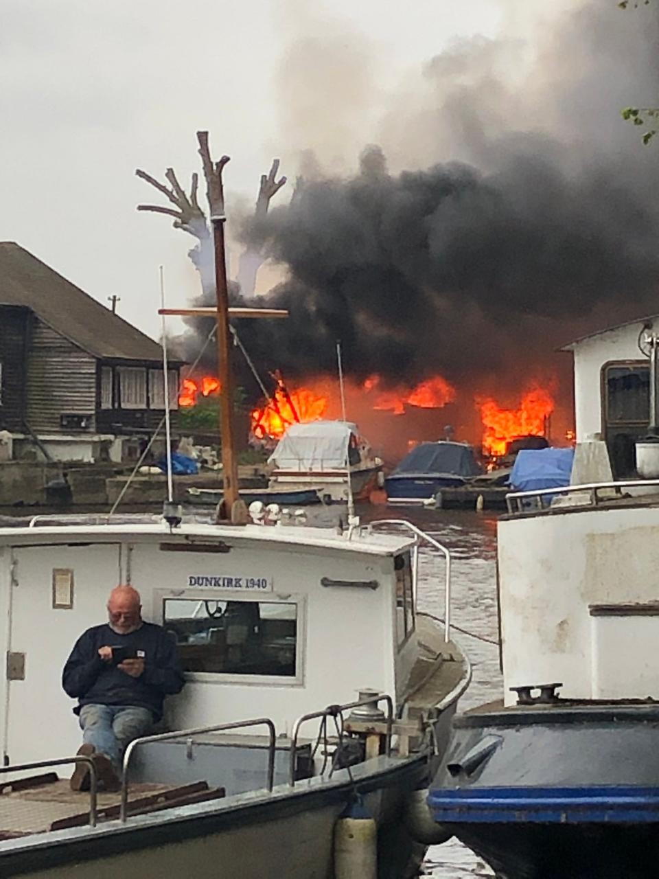 The spirit of Dunkirk: A man checks his phone on a boat as the fire goes on behind him@drbouchard