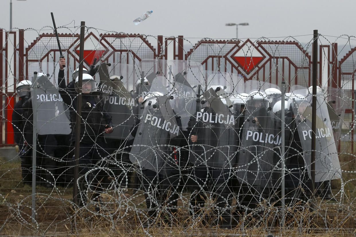 Polish servicemen are seen on the other side of barbed wire fence during clashes between migrants and Polish border guards at the Belarus-Poland border near Grodno, Belarus, on Tuesday, Nov. 16, 2021. Polish border forces say they were attacked with stones by migrants at the border with Belarus and responded with a water cannon. The Border Guard agency posted video on Twitter showing the water cannon being directed across the border at a group of migrants in a makeshift camp. (Leonid Shcheglov/BelTA pool photo via AP)