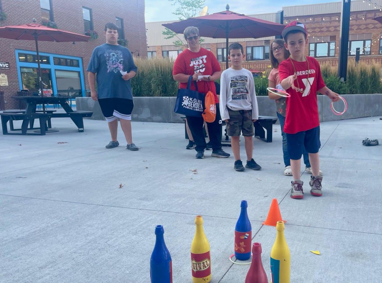 Jason Markey attempts to toss a ring around a bottle in one of several carnival games set up at Market on the Plaza Thursday evening. The games were part of a Back to School Bookswap and Carnival sponsored by Cornerstones Career Learning Center. Participants took gently used books that they could exchange for something different and had an opportunity to participate in carnival games for which the prizes were school supplies. Extra donated books will be donated in the community.